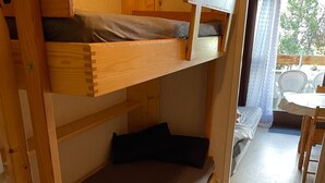 A bunk bed with a lower bunk and a single bed, a small table with chairs, and a view of the outdoors through a window. - Bright studio with mountain view for 4 people (Morillon)