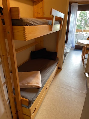 Ein Etagenbett mit unterem Bett und Einzelbett, ein kleiner Tisch mit Stühlen und ein Blick ins Freie durch ein Fenster.