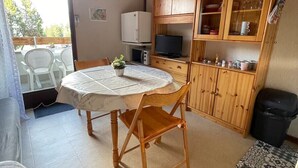 A dining area with a round table, chairs, a television, wooden cabinets, and a trash bin. - Bright studio with mountain view for 4 people (Morillon)