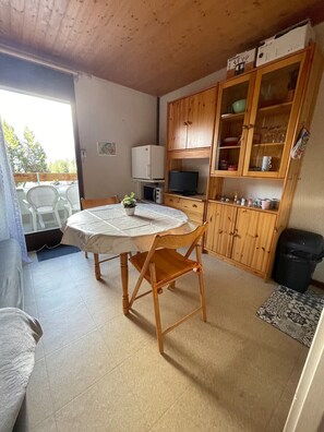 Ein Essbereich mit einem runden Tisch, Stühlen, einem Fernseher, Holzschränken und einem Mülleimer.