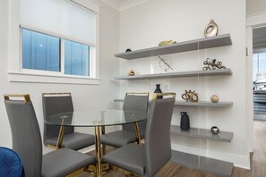 Un comedor moderno con una mesa de vidrio y sillas tapizadas en gris, con detalles dorados y objetos decorativos en estantes flotantes.