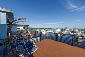 Terraza con una silla colgante, barandilla y vista a un puerto deportivo con barcos.