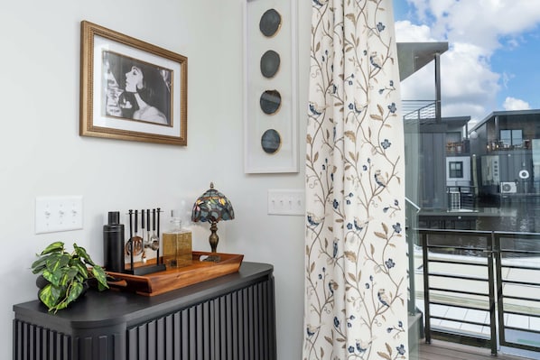 A room with a black console table, a framed photograph, a stained glass lamp, and a window with a view of a building.