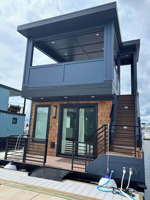 A modern two-story building with a wooden facade, large windows, and a staircase leading to the upper level. - Speakeasy at The Cove Riverwalk Villas (Wilmington)
