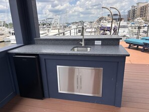 A compact kitchen with a sink, a dishwasher, and a built-in cabinet, overlooking a marina with boats and buildings.
