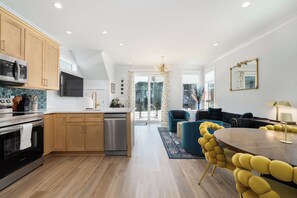 A modern kitchen with a built-in microwave, stove, and dishwasher, leading to a living area with a sofa and a dining table.