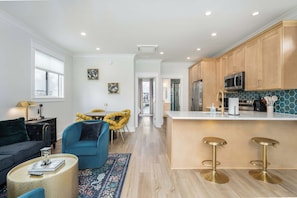 A modern kitchen with wooden cabinets, a central island with stools, and a dining area with a round table and chairs.