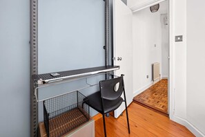 Ein Zimmer mit einem Metallregal, einem schwarzen Stuhl, einem Holzboden und einer weißen Tür.