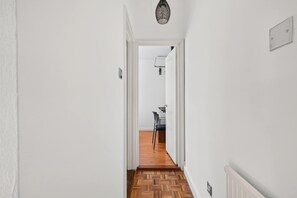 Ein Flur mit weißen Wänden, Holzboden und einer Tür zu einem Zimmer mit einem Sessel und einem Tisch.