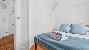 A bedroom with a bed, a wooden floor, a white door, and a wall-mounted light switch. - 1-bed Flat - Fitzrovia - Sleeps 2 (London)