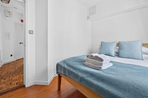 Ein Schlafzimmer mit einem Bett, Holzboden, einer weißen Tür und einem an der Wand montierten Lichtschalter.