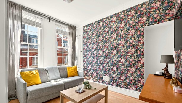 A living room with a sofa, a table, and a floral wallpaper. - 1-bed Flat - Fitzrovia - Sleeps 2 (London)