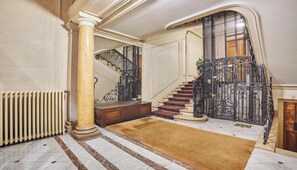 A grand staircase with ornate metal railings, a marble floor, and a beige carpet leading to a landing. - THE ESSENCE OF PARISIAN ELEGANCE ,JUST MOMENTS FROM THE ICONIC ARC DE TRIOMPHE (Paris)