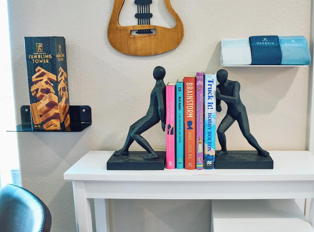 A white shelf with two figurines, a guitar, and books.