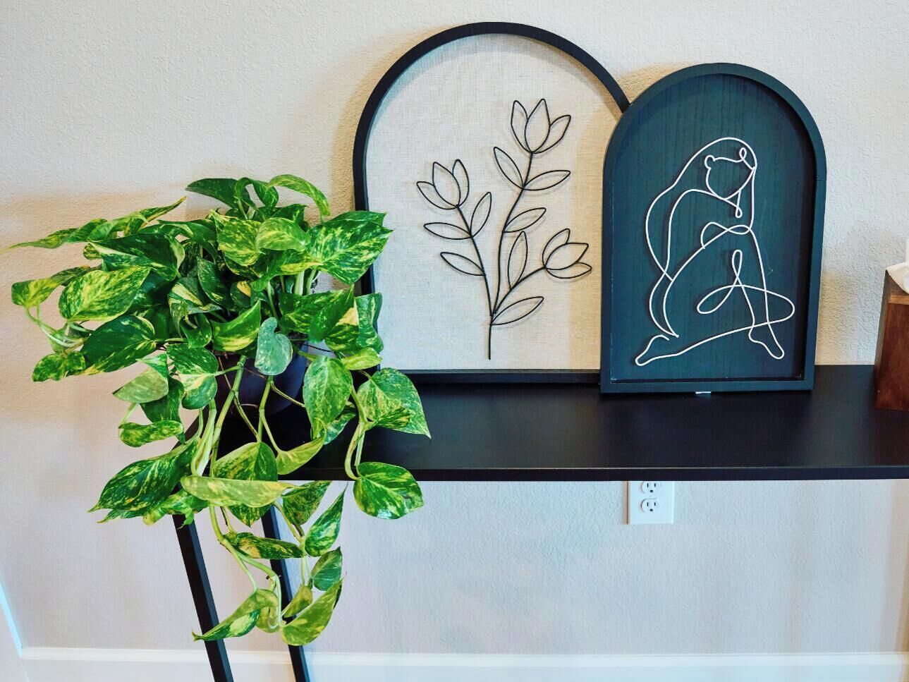 A potted plant, a framed artwork of a plant, and a framed artwork of a person sitting on a bench.