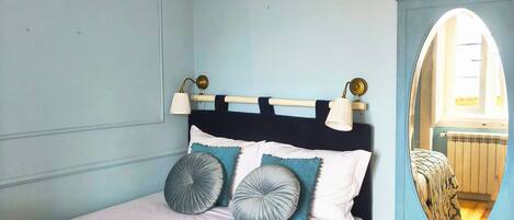 A bedroom with a bed, a bedside table, a mirror, and a window.