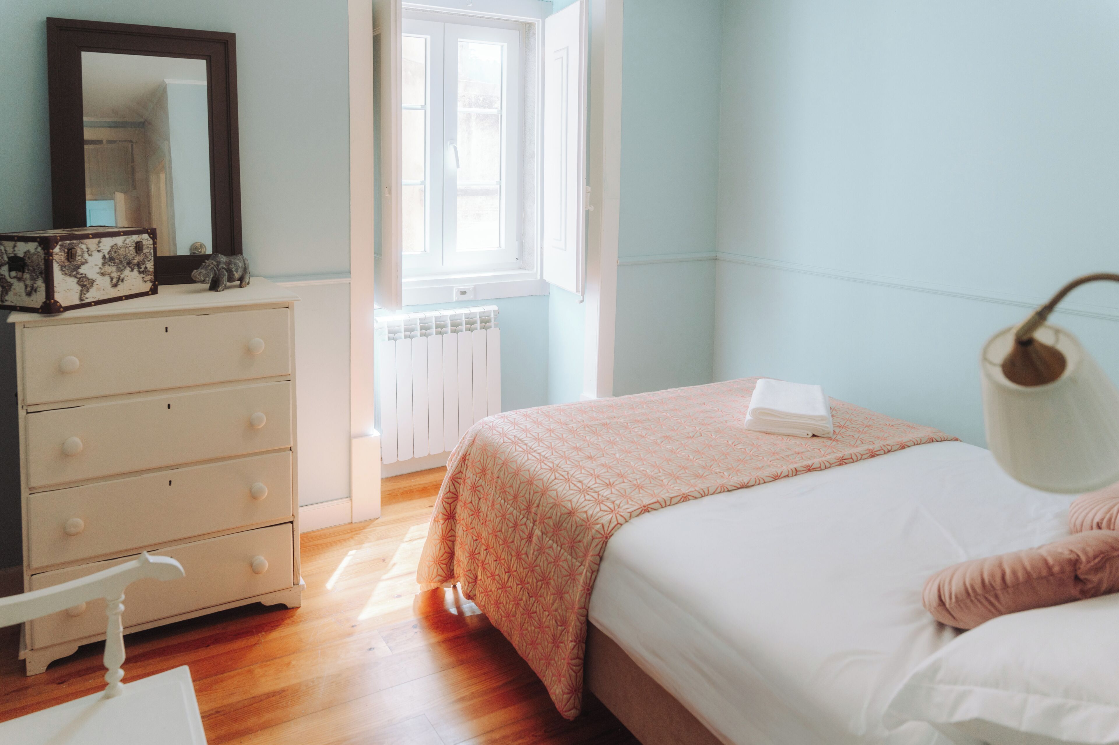 A bedroom with a bed, dresser, mirror, window, and radiator.