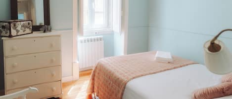 A bedroom with a bed, dresser, mirror, window, and radiator.