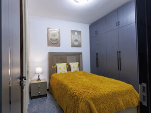Ein Schlafzimmer mit Bett, Nachttisch, Lampe, Kleiderschrank und zwei Wandleuchten.