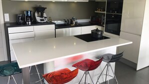 A modern kitchen with white cabinetry, a central island, bar stools, and a built-in oven. - Quiet Villa with Pool - Saint Nolff (Saint-Nolff)