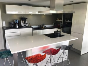 A modern kitchen with white cabinetry, a central island, bar stools, and a built-in oven. - Quiet Villa with Pool - Saint Nolff (Saint-Nolff)