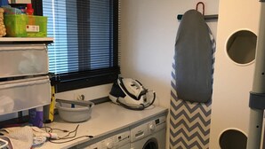 A laundry area with a washing machine, dryer, ironing board, and a window with blinds. - Quiet Villa with Pool - Saint Nolff (Saint-Nolff)