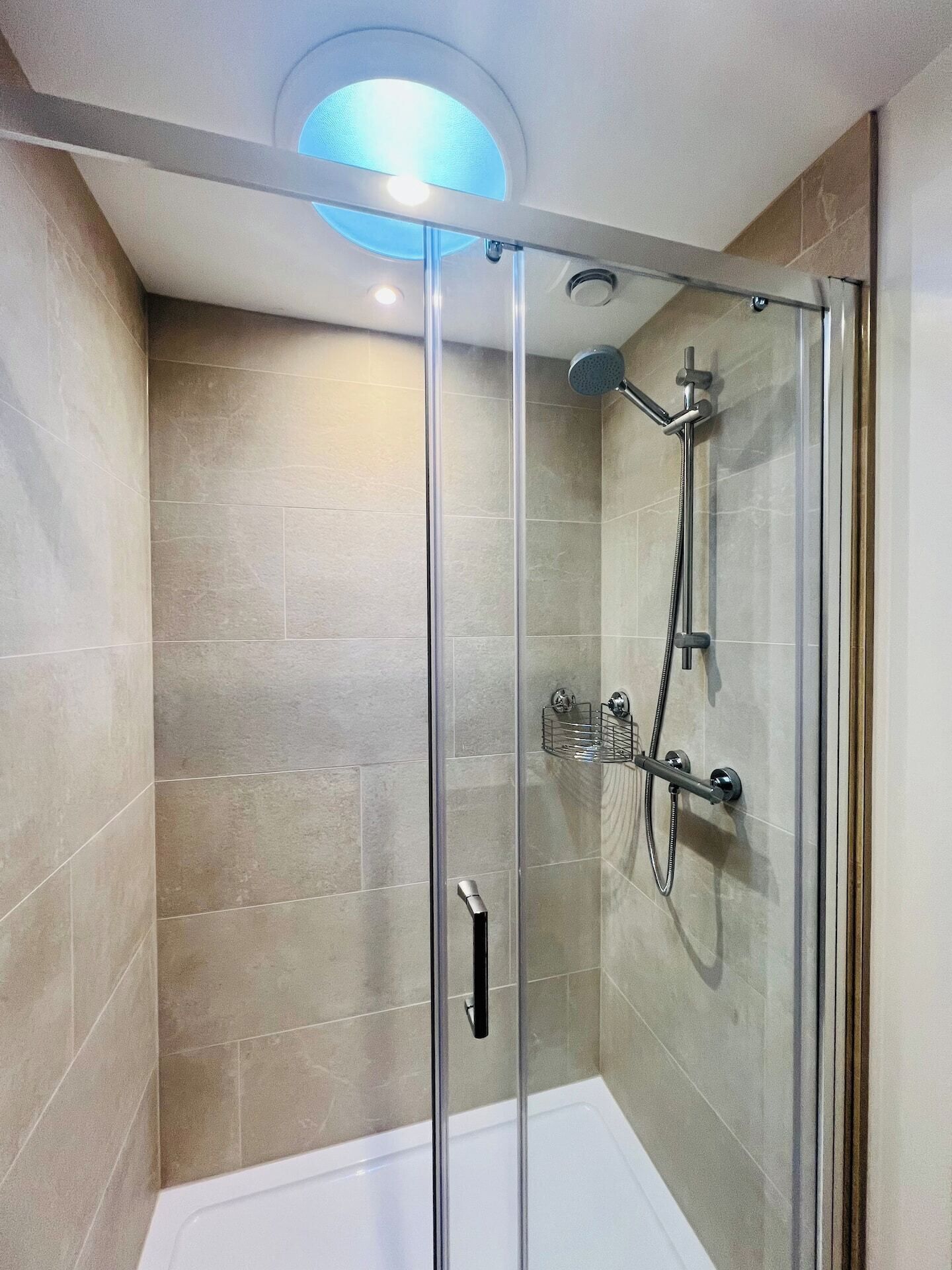 A glass-enclosed shower with a handheld showerhead and a handheld faucet.