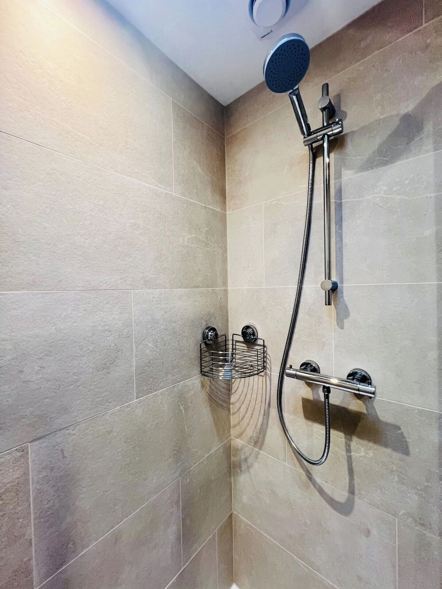 A shower with a handheld showerhead, a wall-mounted faucet, and a metal soap dish.