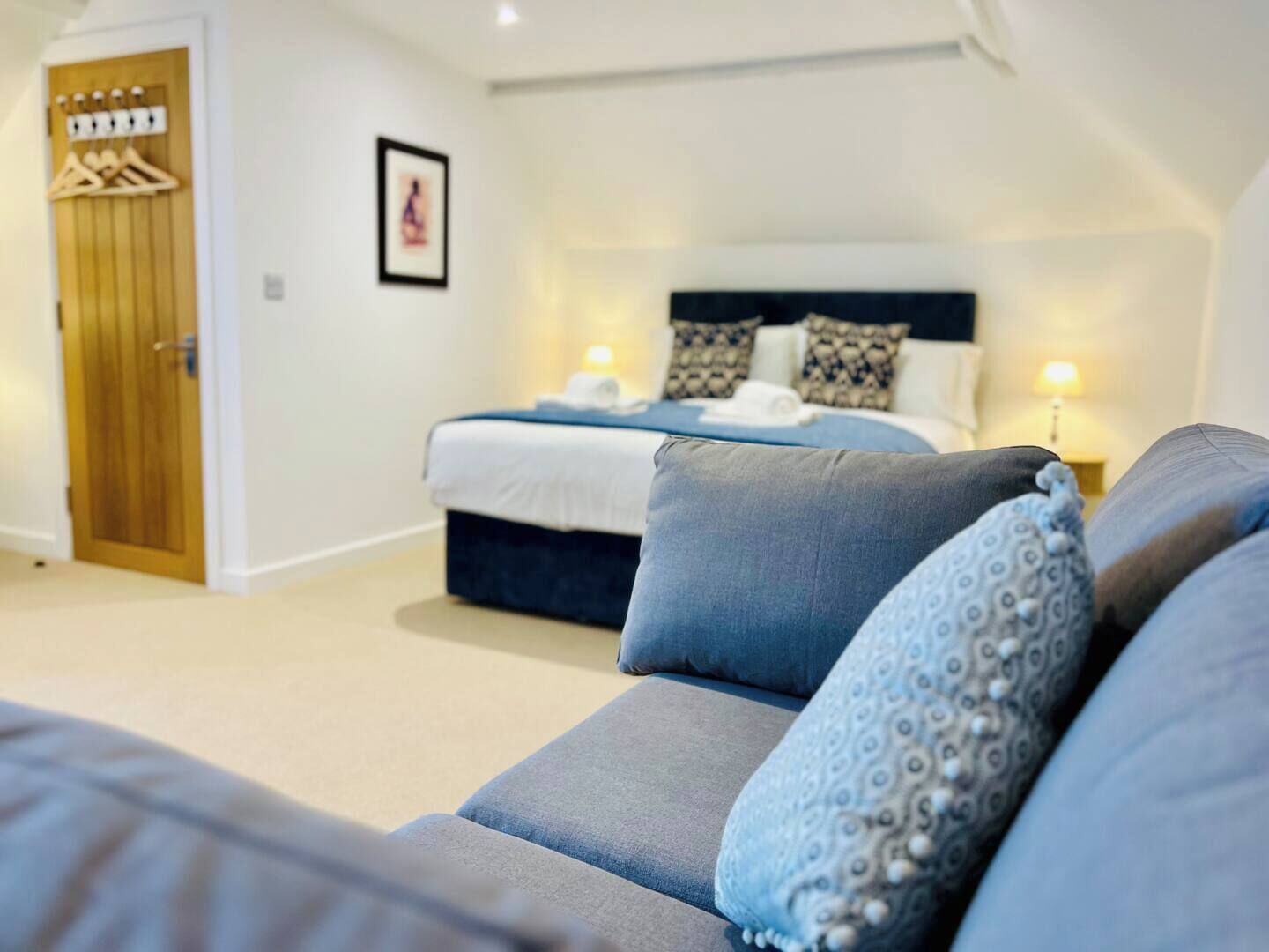 A bedroom with a bed, a sofa, a wooden door, and a wall-mounted light fixture.