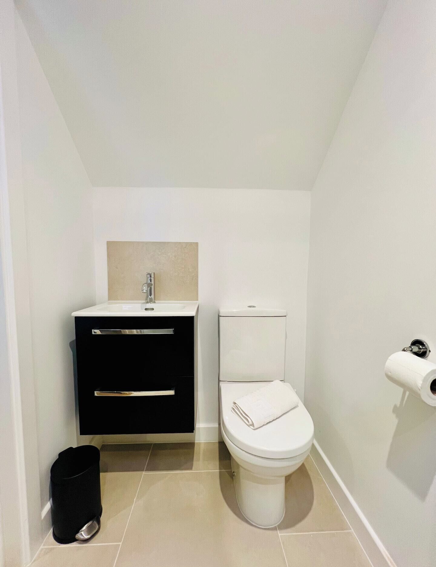 Un baño pequeño y moderno con inodoro, lavamanos y cubo de basura.