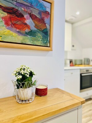 Eine Küche mit einer Holzausziehtheke, einem Blumenstrauß in einer Vase, einer Kerze und einem farbenfrohen abstrakten Gemälde an der Wand.