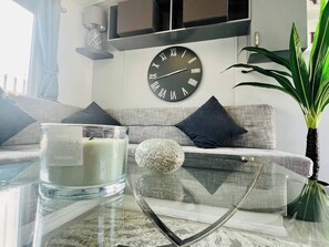 Una sala de estar moderna con un sofá, una mesa de vidrio con una vela, una piedra decorativa y un reloj de pared.