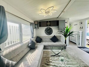 Ein modernes Wohnzimmer mit einer Couch, einem Glastisch, einer Wanduhr und einer Deckenleuchte.