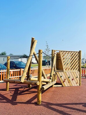 Ein Spielplatz mit hölzernen Klettergerüsten und einer roten, gummiartigen Oberfläche.