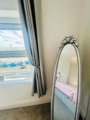 Ein Zimmer mit großem Fenster, Spiegel und einem Bett.