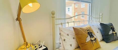 A bedroom with a bed, a bedside lamp, a window with a view of buildings, and a small table with a lamp.