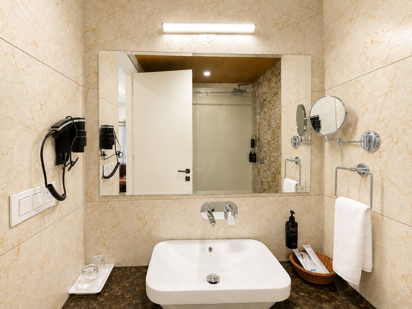 Un baño con lavamanos blanco, un espejo, toallero y zona de ducha.