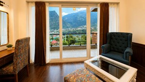 A room with a large sliding glass door, a chair, a sofa, and a small table. - The himalayan chester (Manali)