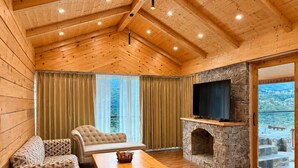 A wooden interior with a stone fireplace, a sofa, a chair, and a television. - The himalayan chester (Manali)