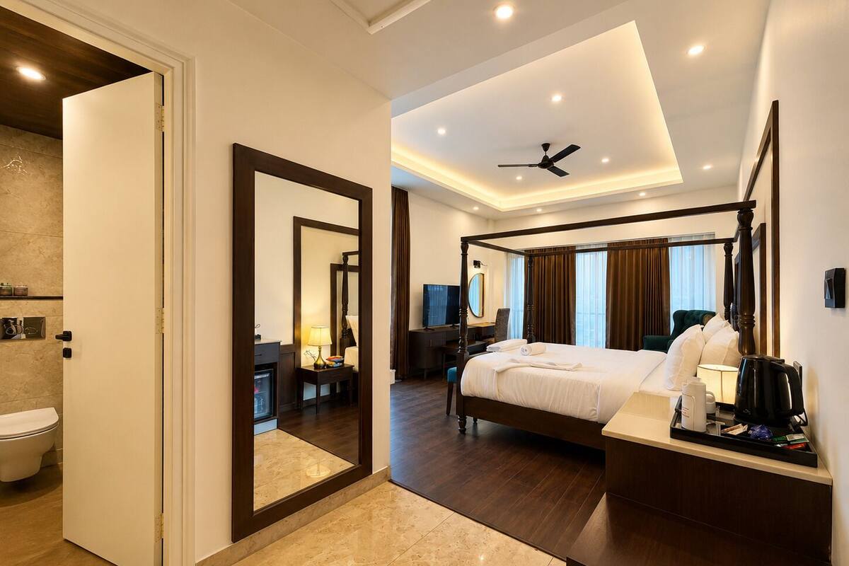 A hotel room with a four-poster bed, a sitting area with a desk and chair, a television, and a bathroom with a toilet and sink.