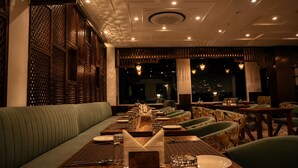 A restaurant with a long dining table, cushioned seating, and a view of the city at night.