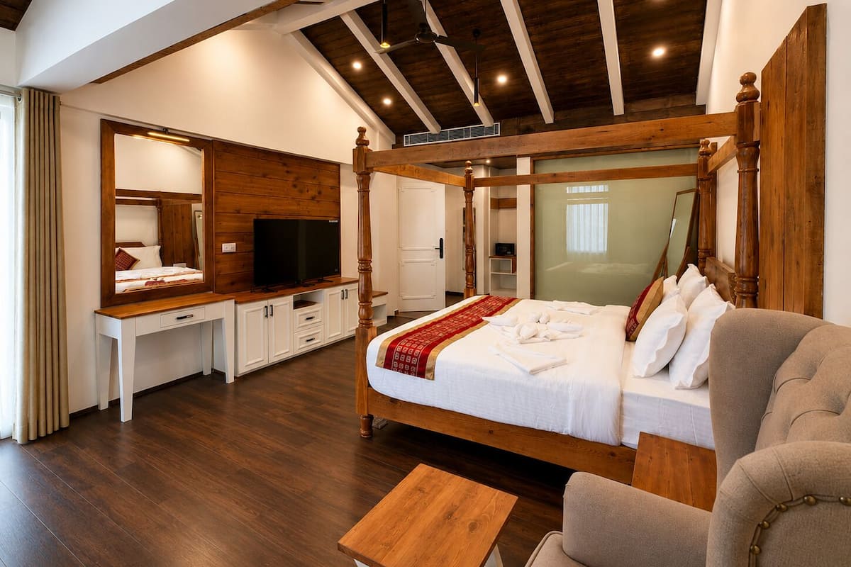 A bedroom with a four-poster bed, a desk with a TV, and a chair.