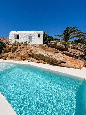 A white building with a pool, surrounded by rocks and palm trees. - Villa Delos Mystique Mykonos (Mykonos)