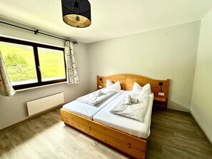 Ein Schlafzimmer mit einem Holzbett, einem Fenster mit Blick ins Grüne und einer Deckenleuchte.