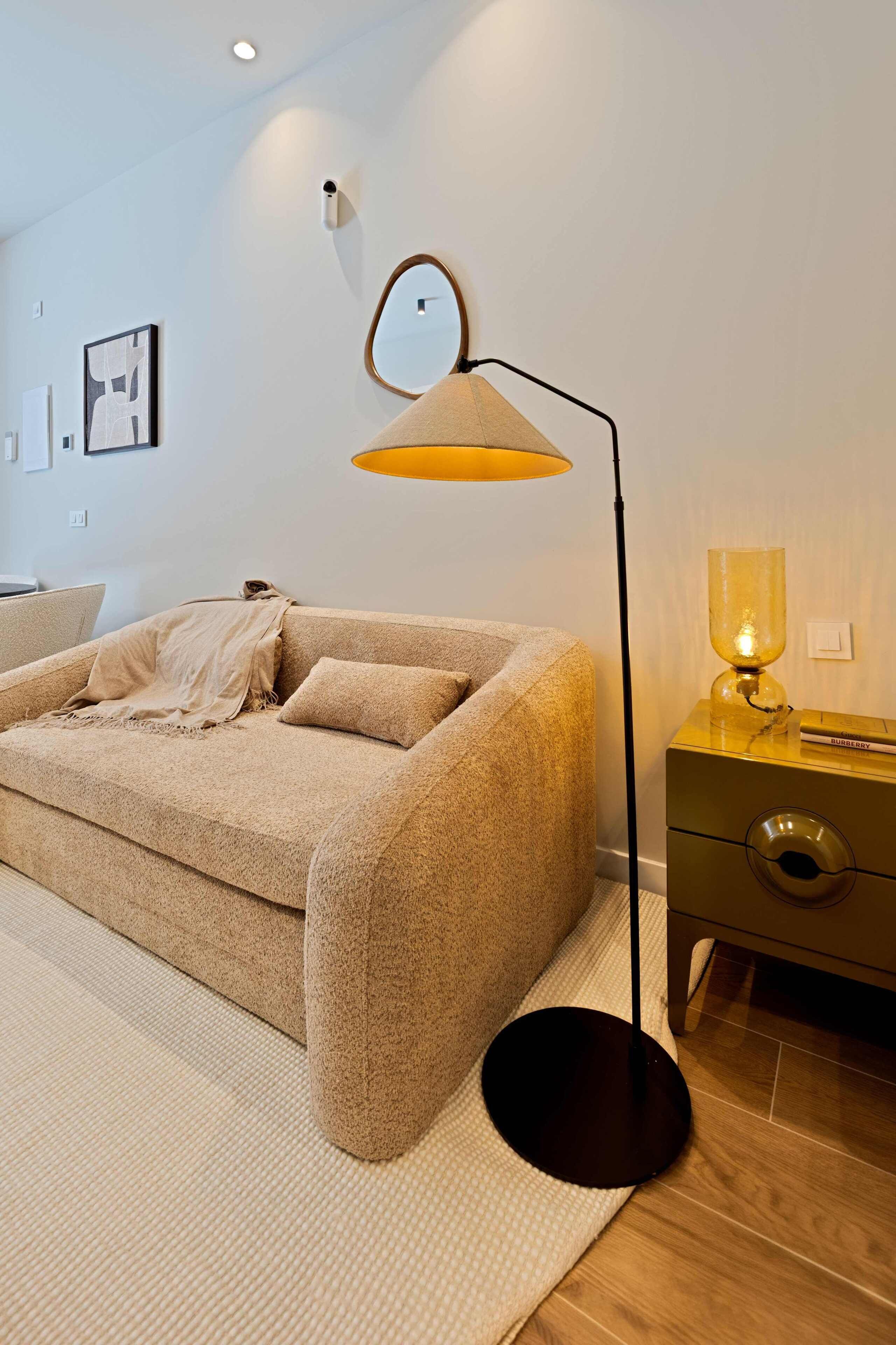 Ein modernes Wohnzimmer mit einer Couch, einer Stehlampe, einem Beistelltisch mit Lampe und einer Wandleuchte.