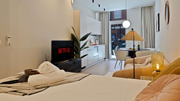 Una camera d'hotel moderna con un letto, una TV che mostra Netflix, un'area ristoro e vista sulla città.