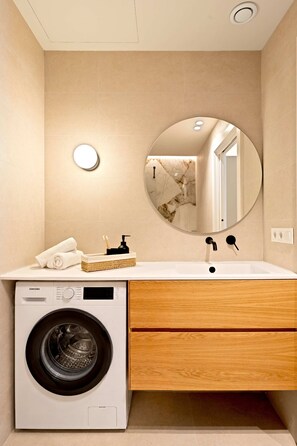Ein modernes Badezimmer mit integrierter Waschmaschine, einem runden Spiegel und einem hölzernen Waschtisch.