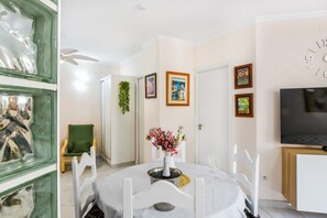 Un coin repas avec une table ronde, des chaises, un vase de fleurs, un téléviseur et des tableaux encadrés accrochés au mur.