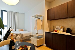 A hotel room with a bed, a small kitchenette, a glass partition, and a dining area with a table set for two. - SariStays VLC Vida Suites (València)