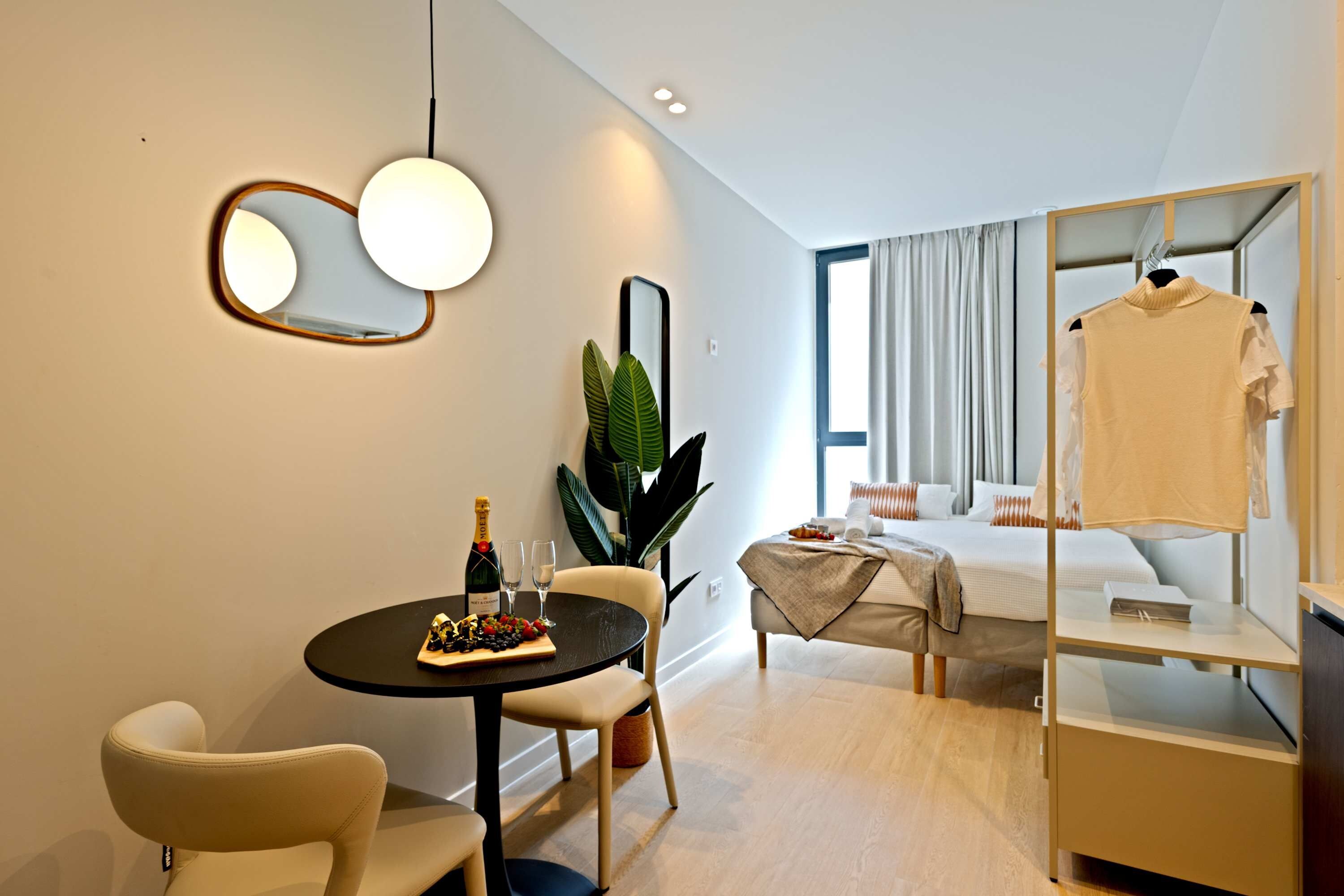 Moderni hotellihuone, jossa on ruokailutila, näköalalla varustettu sänky, peili ja vaateteline.